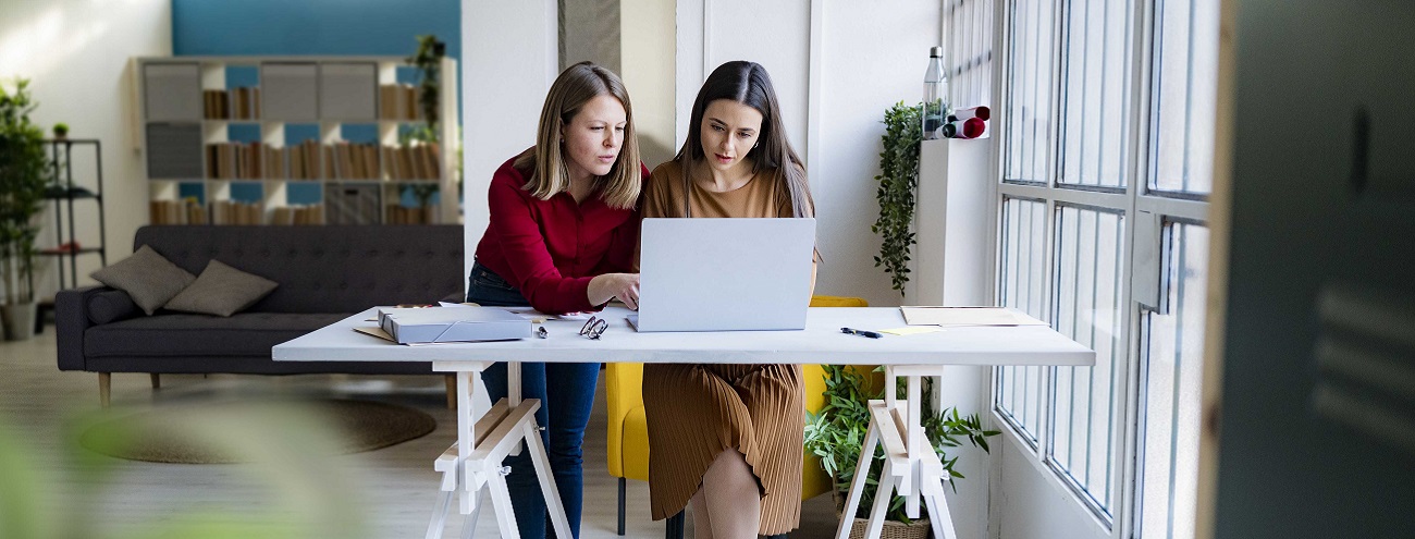 EU-Förderungen für Gründer und etablierte Unternehmen aus IBW/EFRE & JTF tragen zu Wachstum und Innovation bei. 2 junge Gründerinnen sitzen in modernem Büro-Loft an einem Hochtisch vor einem Laptop, als Beispiel für EU-Förderungen zur Stärkung der Wettbewerbsfähigkeit in Österreich