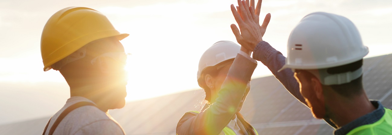 Drei Arbeiter mit Schutzhelm stehen vor einer PV-Anlage und feiern mit High-five deren Fertigstellung - ist ein Symbol für EU-Förderungen aus dem Fonds für einen gerechten Übergang.