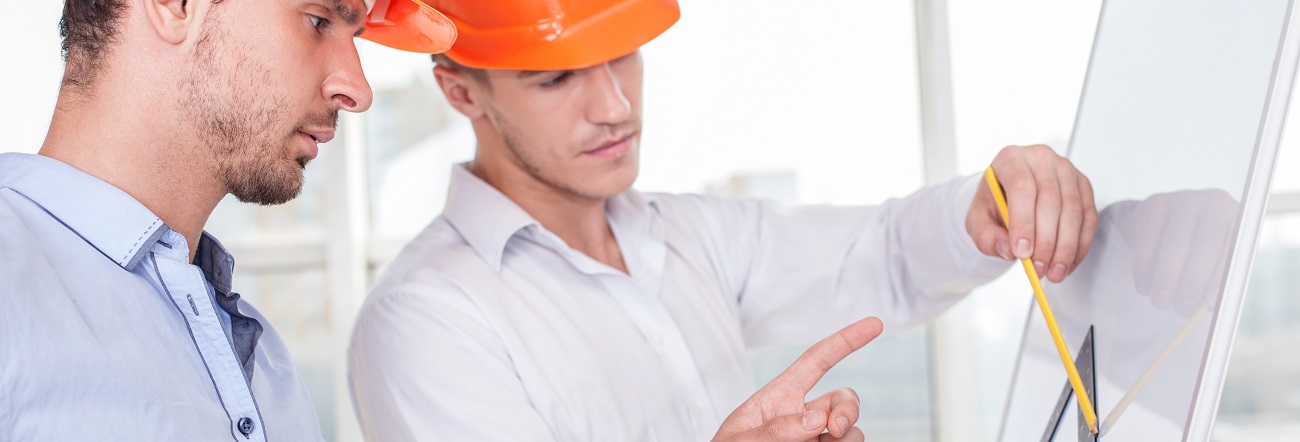 Zwei Architekten mit Schutzhelmen zeichnen mit Lineal auf einem stehenden Zeichenbrett